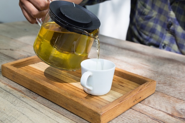 gießt heißen Tee in die weiße Tasse