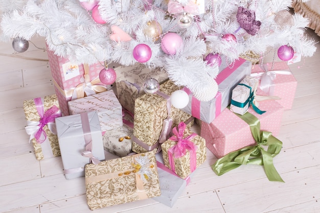 Giftboxes, bolas de decorações de natal-de-rosa e branco pendurado em uma árvore de natal branca decorativa