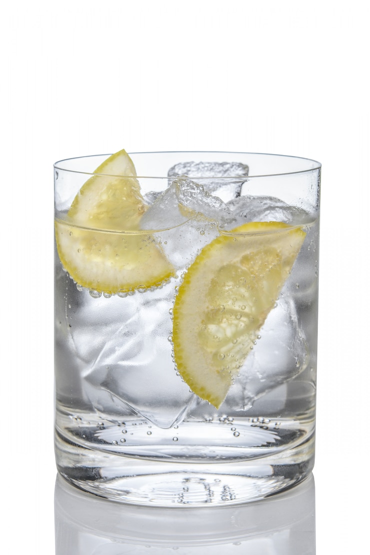 Foto gim e tónico do cocktail com o limão e o gelo isolados no branco.