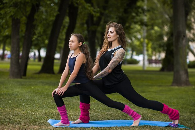 Gimnasia de trabajo en equipo familiar. Estilo de vida de las mujeres activas. Ejercicio de yoga al aire libre, belleza saludable, deporte adolescente con entrenador. Fondo de naturaleza, entretenimiento exterior.