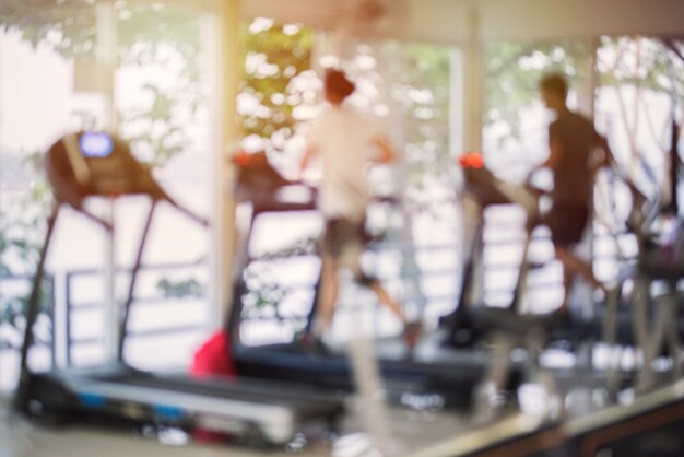 Gimnasio borroso con máquinas cardiovasculares y equipo de entrenamiento de fuerza y peso. Figuras de humanos corriendo en cintas de correr en el gimnasio.