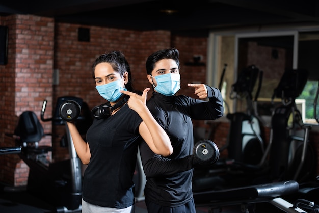 Gimnasio después de la corona: joven pareja india que hace ejercicio en el gimnasio después del brote de corona y usa una mascarilla protectora