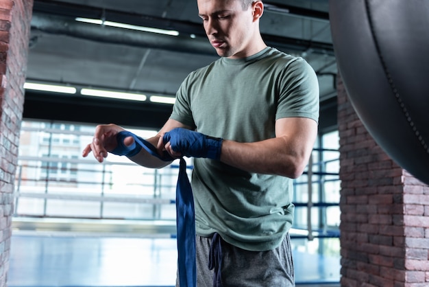 Gimnasio espacioso. Luchador fuerte guapo vistiendo camiseta caqui entrenando duro en un gimnasio espacioso y ligero