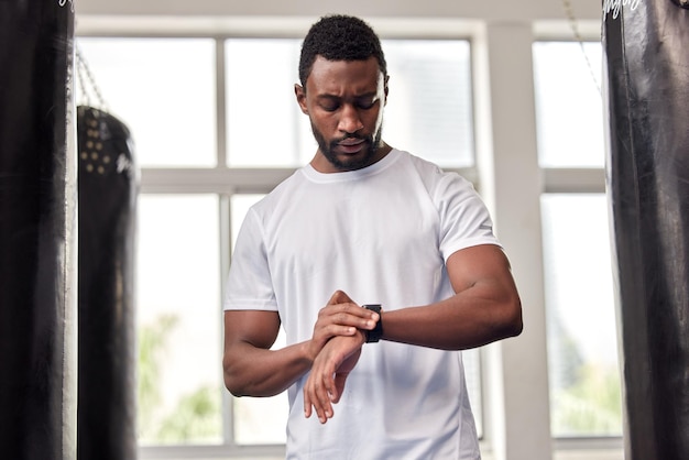 Gimnasio y hombre negro con reloj inteligente para la aplicación de salud del tiempo o seguimiento de objetivos de bienestar Entrenamiento deportivo y atleta masculino serio que usa tecnología para monitorear objetivos de entrenamiento o ejercicio