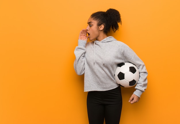 Gimnasio joven mujer negra susurrando matices de chismes. Sosteniendo un balón de fútbol.