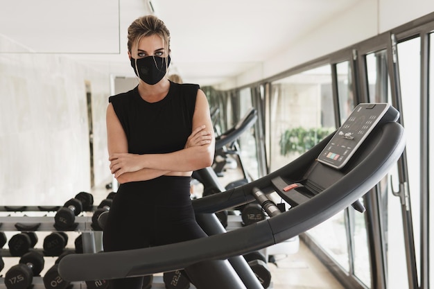 Gimnasio nuevo normal. Joven atlética con una mascarilla de prevención durante su entrenamiento físico.