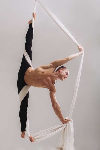 Gimnasta masculino haciendo la división con cintas de seda aéreas.