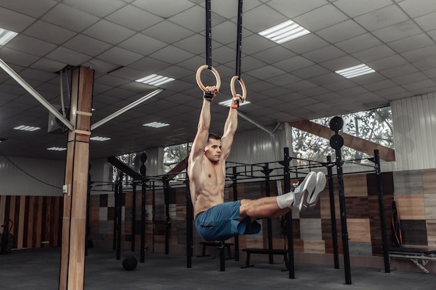 Gimnasta masculino musculoso haciendo ejercicio en anillos de gimnasia en un club de salud moderno. Concepto de estilo de vida saludable