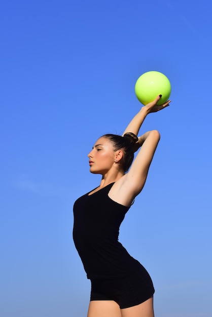 Gimnasta mujer en ropa deportiva negra con bola verde.