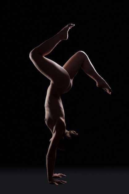Foto gimnasta nua posando em um estúdio escuro em mãos