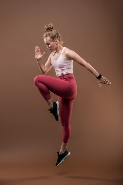 Foto gimnasta o ejecutante en forma bonita en ropa deportiva manteniendo una pierna doblada en la rodilla y doblando el brazo derecho en el codo mientras baila