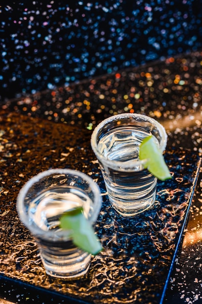 Gin oder Wodka mit Limette. Zwei Gläser mit einem Cocktailalkohol mit Zitronen auf der schwarzblauen Oberfläche. Wodka, Cocktail, Alkohol, Getränke, Restaurant, Entspannungskonzept.