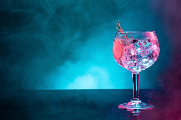 Gin tonic frío bajo iluminación de luz rosa y azul sobre fondo ahumado con espacio de copia