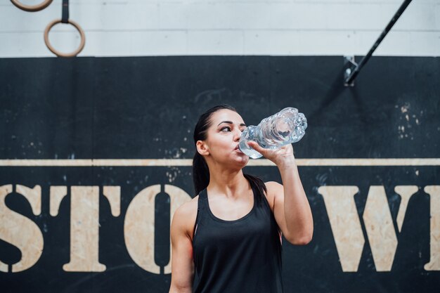 Foto ginásio indoor de jovem mulher esportiva, recuperando a água potável