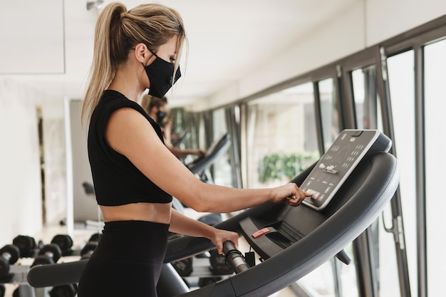 Ginásio novo normal. Jovem mulher atlética usando uma máscara de prevenção durante seu treino de fitness.