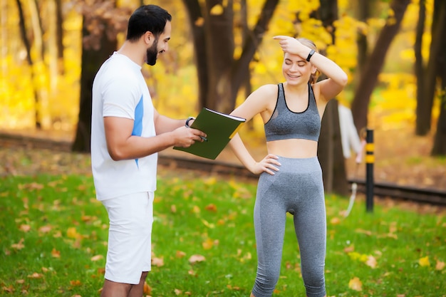 Ginástica. Treinador pessoal toma notas enquanto mulher exercitando ao ar livre