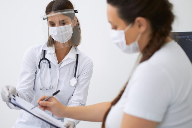 Ginecologista e paciente do sexo feminino usando máscaras protetoras médicas durante o diagnóstico