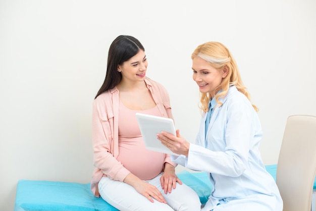 Ginecologista obstetra e mulher grávida usando tablet juntos