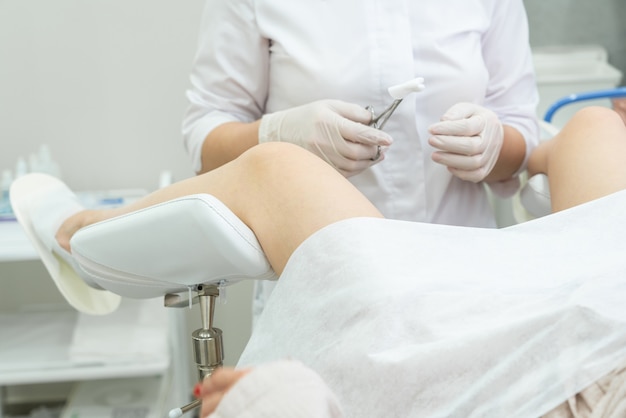 Ginecólogo profesional examinando paciente femenino en silla ginecológica con pinzas