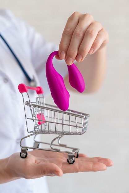 El ginecólogo sin rostro recomienda comprar un vibrador vaginal clitoridiano para mantener la salud de la mujer El médico sostiene un mini carrito y un masturbador para orgasmos intensos