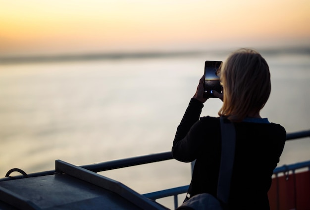 Girl Tourist fotografiert einen Liner bei Sonnenuntergang auf dem See in Norwegen Tourist nimmt Sonnenuntergang am Telefon