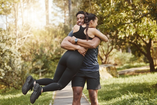 Foto giro físico y abrazo de pareja en el parque al aire libre para hacer ejercicio y correr para hacer ejercicio cardiovascular. citas, hombres y mujeres felices e interraciales se abrazan para el bienestar, el cuerpo sano y los deportes.