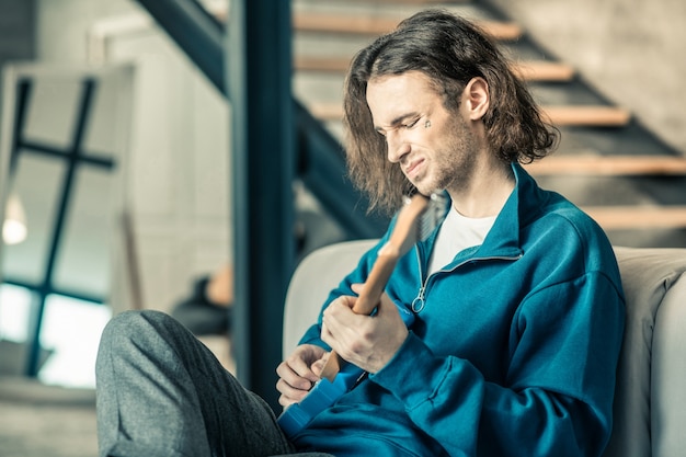 Gitarrenkenntnisse. Dunkelhaariger junger Mann, der mit dem Klang seiner Gitarre unzufrieden ist, während er ein Musikinstrument stimmt