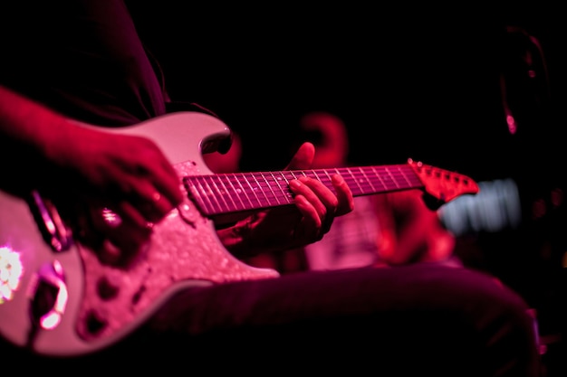 Gitarrist spielt E-Gitarre, Nahaufnahme der Gitarre und Hände, rote Beleuchtung