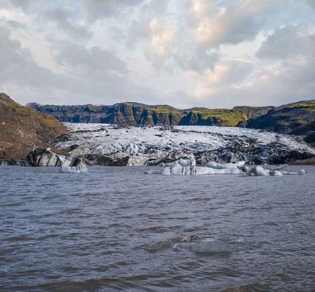 Glaciar Solheimajokull no sul da Islândia A língua desta geleira desliza do vulcão Katla Bela lagoa glacial com blocos de gelo e montanhas circundantes Pessoas irreconhecíveis