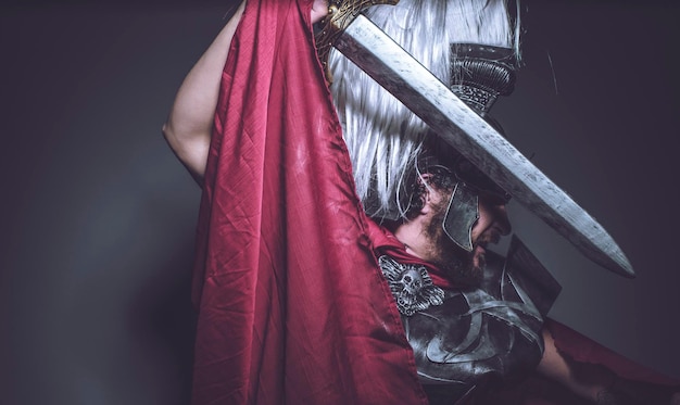 Foto gladiador romano, luchador y guerrero de roma con casco y manto rojo, porta espada de hierro, barba y pelo largo.