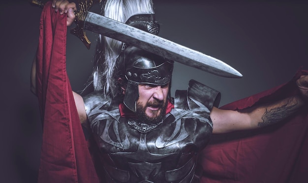 Gladiador romano, luchador y guerrero de Roma con casco y manto rojo, porta espada de hierro, barba y pelo largo.