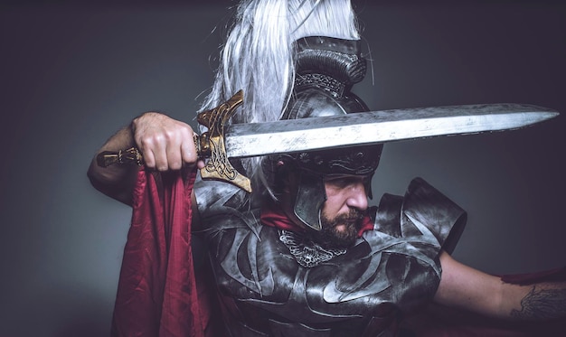 Foto gladiador romano, luchador y guerrero de roma con casco y manto rojo, porta espada de hierro, barba y pelo largo.