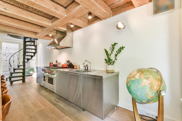 Glänzende Chromschränke und Geräte der modernen Küche im Landhaus mit Holzbalkendecke und Wendeltreppe