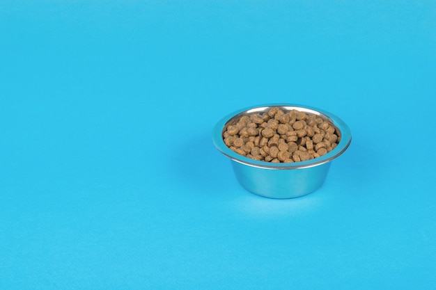 Glänzende Metallschüssel gefüllt mit Hundefutter auf blauem Hintergrund