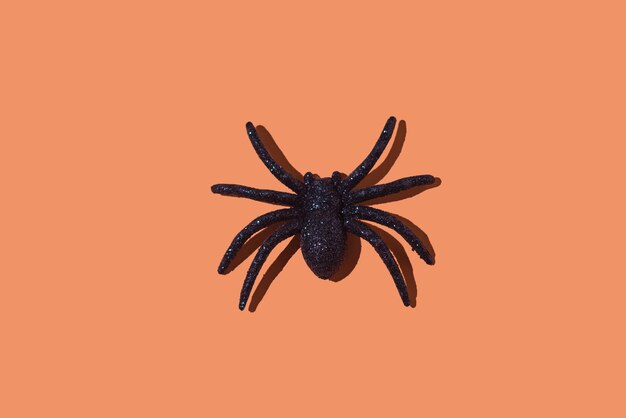 Foto glänzende plastikspinne als dekoration für halloween auf einem orangefarbenen hintergrund konzept des terrors phobie angst feier arachnophobie tag der toten ekel abstoßungsmittel und spielzeug