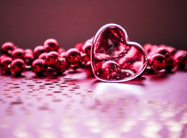 Glänzendes transparentes Herz und eine Gruppe von roten Perlen Perfekter Valentinstag-Grußkartenhintergrund Horizontales Bild in rosa Ton