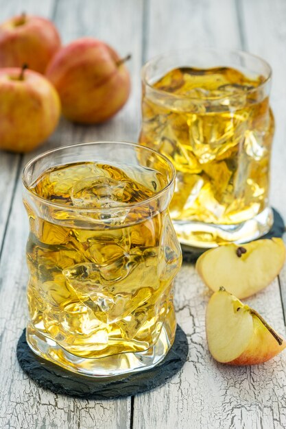 Gläser Apfelsaft mit Eis und frischem rotem Apfel auf einem Holztisch an einem Sommertag.