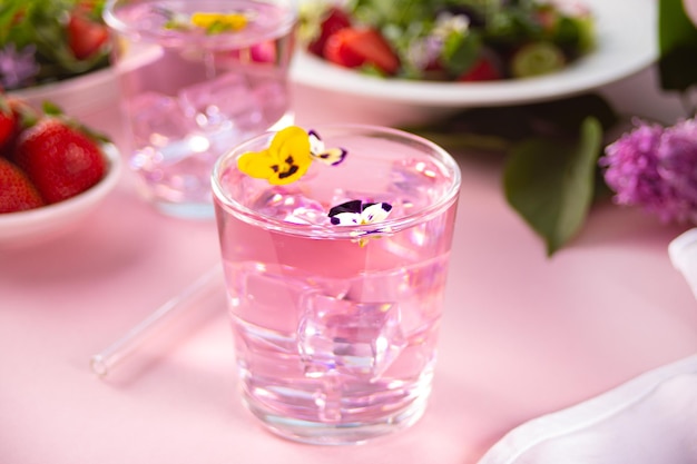 Gläser aus rosafarbenem, violettem, violettem Cocktail, verziert mit Blumen, Viola-Stiefmütterchen und frischem Salat auf dem Hintergrund