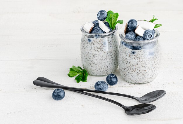 Gläser Chiasamenpudding mit Blaubeeren und Kokosnuss auf weißer Holzwand. Speicherplatz kopieren. Superfood-Konzept.