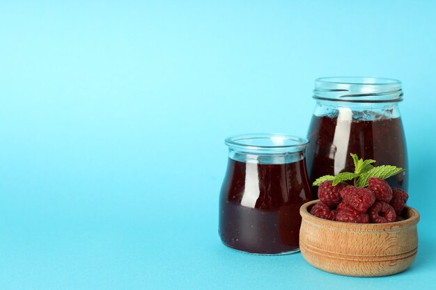 Gläser Himbeermarmelade mit Zutaten auf blauem Hintergrund