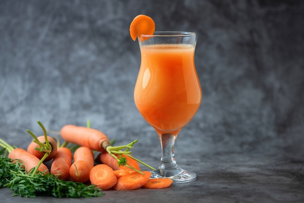 Gläser Karottensaft mit Gemüse auf grauem Tisch.