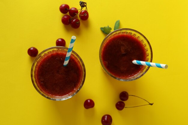 Gläser Kirsch-Smoothie und Zutaten auf gelbem Hintergrund