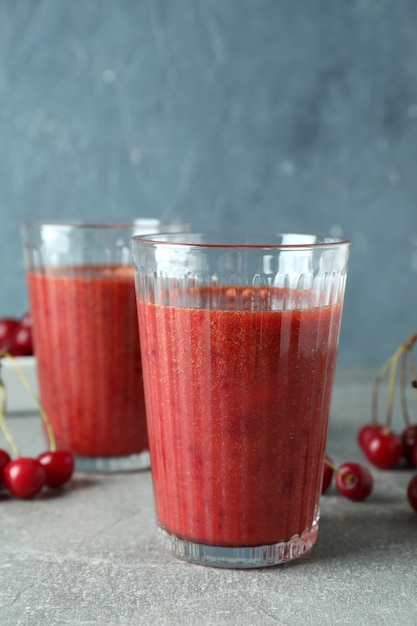 Gläser Kirsch-Smoothie und Zutaten auf grauem strukturiertem Tisch