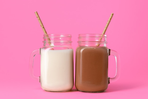 Gläser mit aromatisierten Milchshakes vor rosa Hintergrund