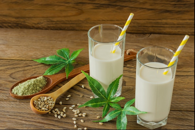 Gläser mit Cannabis pflanzlichem veganem Gluten und laktosefreier Milch und Cannabisblättern auf Holztisch.