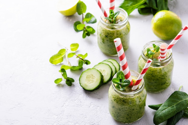 Gläser mit grünem Smoothie und roten Tubuli auf hellem Hintergrund.