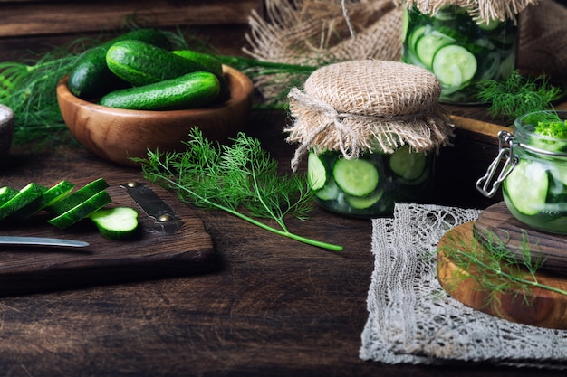 Gläser mit hausgemachten eingelegten Gurken, in Scheiben geschnitten mit Dill und Knoblauch auf rustikalem Holz