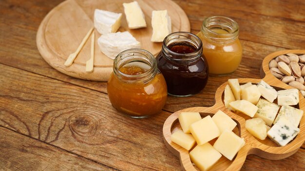 Gläser mit hausgemachten Marmeladen und verschiedenen Käsesorten auf einem Holztisch Käseplatte