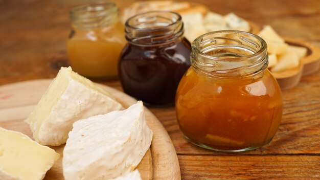 Gläser mit hausgemachten Marmeladen und verschiedenen Käsesorten auf einem Holztisch Käseplatte