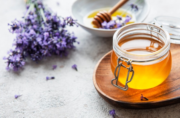 Gläser mit Honig und frischen Lavendelblüten auf Betonhintergrund